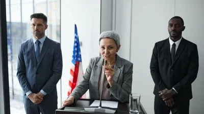 Muž v obleku pred mikrofónmi na tlačovej konferencii
